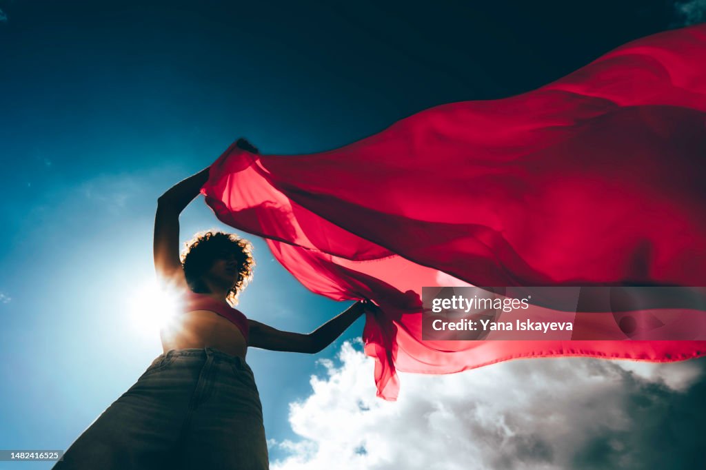 A silhouette of a young woman waving a red flag against the blue skies
