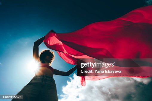 A silhouette of a young woman waving a red flag against the blue skies