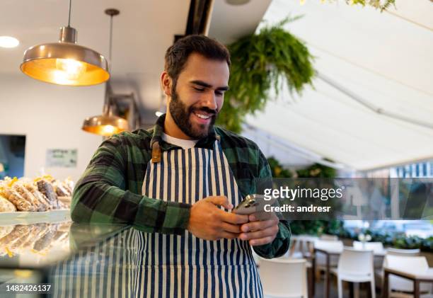 kellner arbeitet in einem café und benutzt sein handy während seiner pause - small business phone stock-fotos und bilder