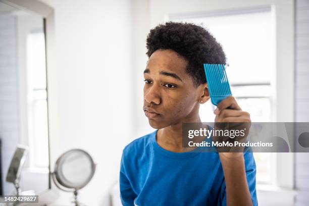 teenage boy combing his hair in mirror of his bathroom - combing foto e immagini stock