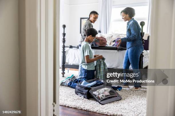 lesbian couple and teenage son packing suitcases in bedroom for vacation - teen packing suitcase stock pictures, royalty-free photos & images
