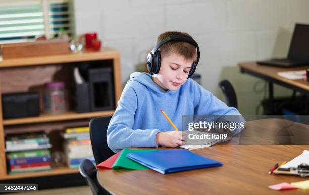 student writing, wearing noise-cancelling headphones - cancelamento imagens e fotografias de stock