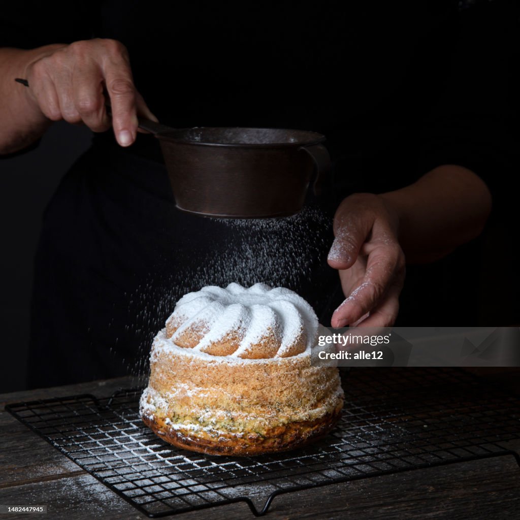 Weibliche Hand, die Puderzucker auf den Kuchen streut