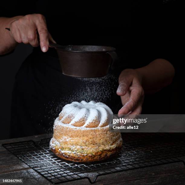 female hand sprinkling icing sugar on cake - poedersuiker stockfoto's en -beelden