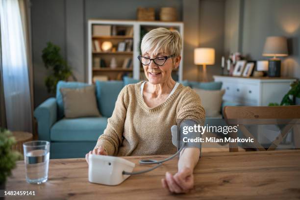 年金受給者の年配の女性がデジタルメーターで血圧を測定します - high blood pressure ストックフォトと画像