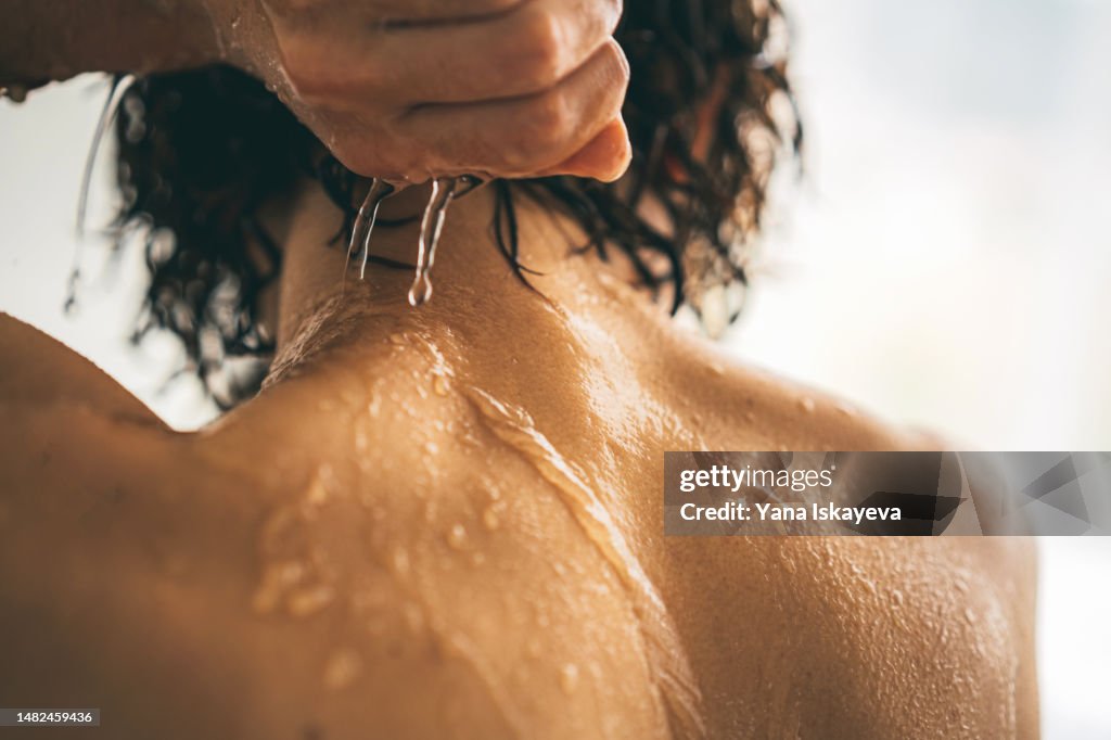 Asian woman with short hair is taking a shower or a bath, water running down her neck and back, healthy young skin texture closeup