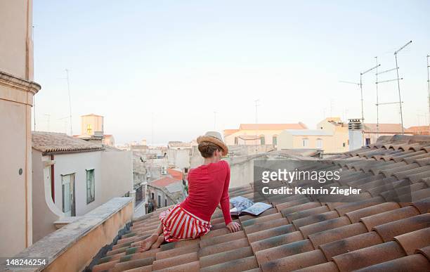 woman sitting on a tiled roof, reading cookbook - city book stock pictures, royalty-free photos & images