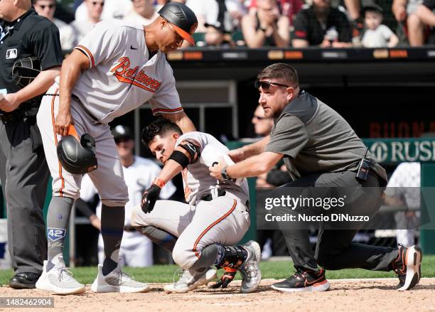 Ramon Urias of the Baltimore Orioles is helped up by a team athletic trainer and first base coach Anthony Sanders of the Baltimore Orioles after he...