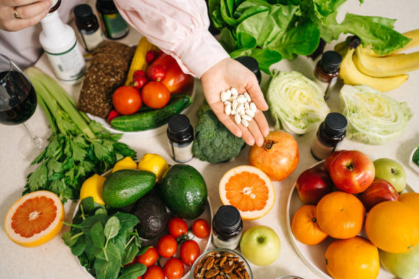 in the dietitian's office, the table is set with vegetables, fruits, nuts, bread, herbs, capsules of drugs in the palm - plants and supplements stock pictures, royalty-free photos & images