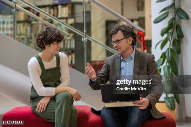 ein mann und eine frau sitzen und unterhalten sich in der lobby eines bürogebäudes - debatte stock-fotos und bilder