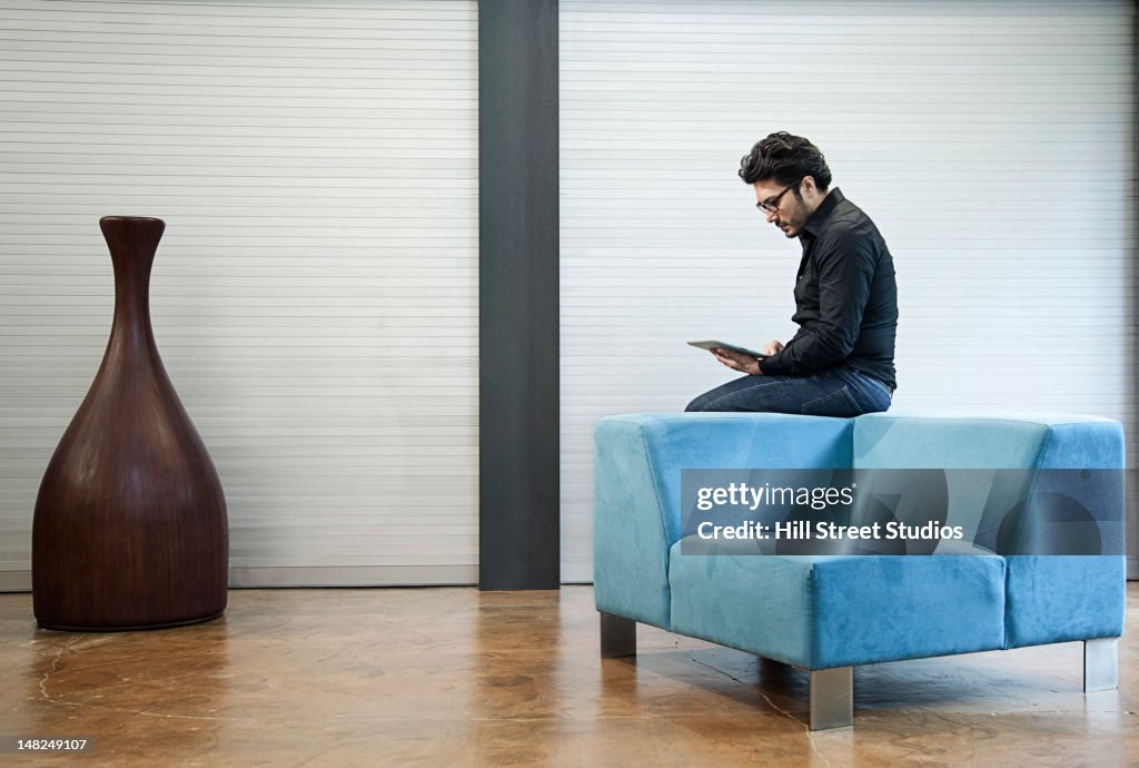 Hispanic man sitting on chair using digital tablet