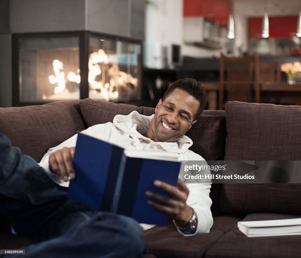 Mixed race man laying on sofa reading book