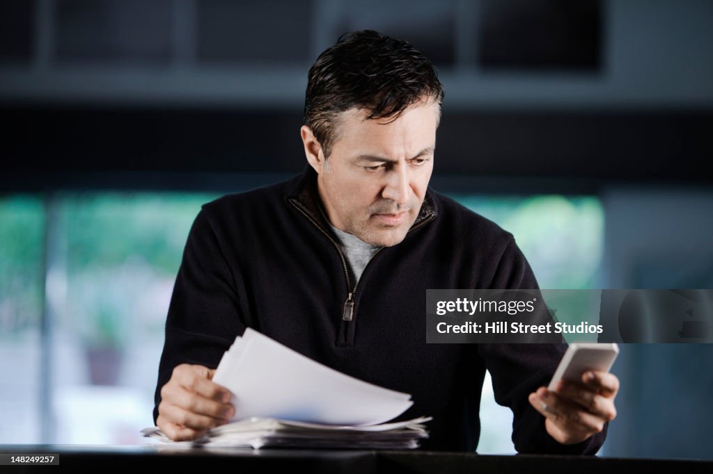 Hispanic businessman using cell phone and looking at paperwork