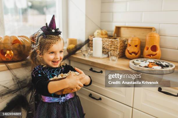 happy laughing baby girl with bowl of popcorn on kitchen, decorated for halloween - naughty halloween stock pictures, royalty-free photos & images