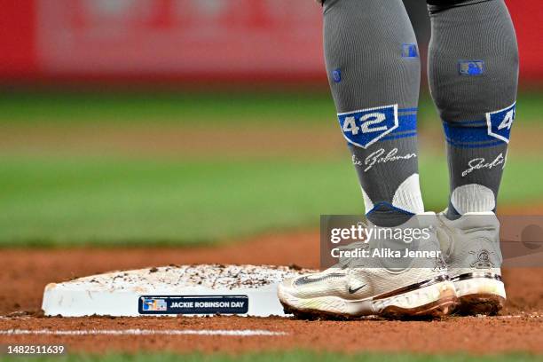 Kolten Wong of the Seattle Mariners wears Stance socks with commemorative “42” logo, Nike "42" shoes, while standing on first base with a placard in...