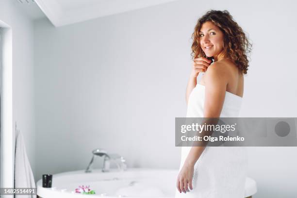 preparing for a spa day for women - beautiful curly woman in towel prepare taking a spa treatment in the foam water bath. - envuelto en una toalla fotografías e imágenes de stock