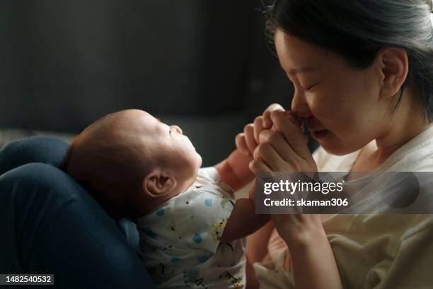 close-up shot of an asian young adult mother embracing and kissing her baby with soft light and a warming moment - changing form photos et images de collection