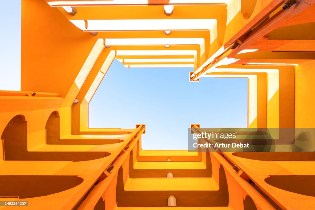 Visual yellow architecture with inner courtyard lightwell from directly below, blue sky and creative perspective.