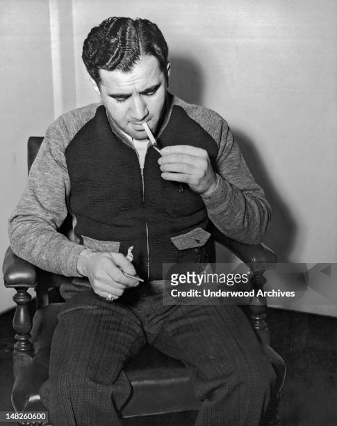 Abe Reles lighting a cigarette at the District Attorney's office in Brooklyn, New York, New York, 1940. He was considered the most feared hit man for...