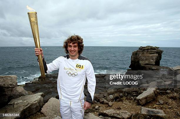 In this handout image provided by LOCOG, Torchbearer 001 Thomas Mules holds the Olympic Flame on Pulpit Rock, Portland Bill, at the beginning of Day...