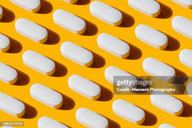 repeated white pills pattern calcium capsule on yellow background - pill background stock pictures, royalty-free photos & images