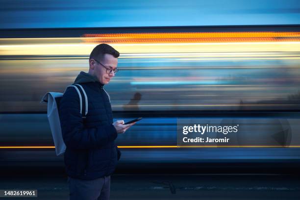 man with backpack holding and using phone against tram in blurred motion - transports-publics photos et images de collection