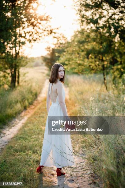 young woman, holding red book, and walking by the footpath - twilight book stock pictures, royalty-free photos & images