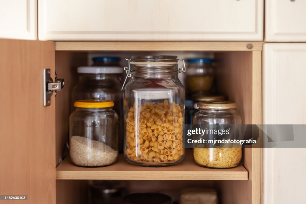 Botes de cristal llenos de pasta y arroz en un armario de la despensa