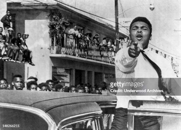 American boxer Cassius Clay points at the camera from an open car door as he takes part in a pre-football game parade, Miami, Florida, December 14,...