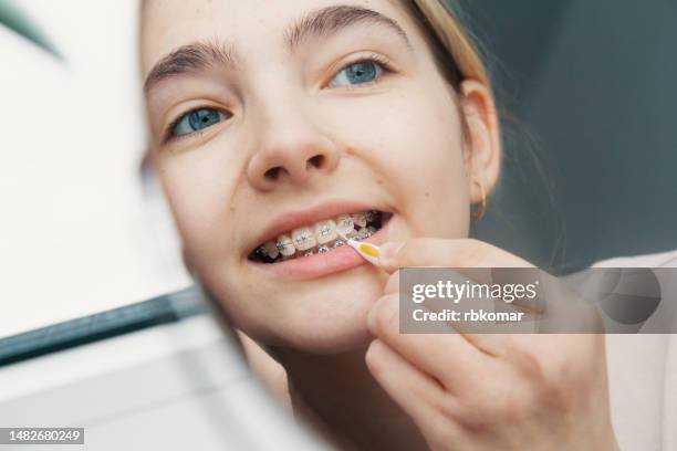 brushing braces with a interdental brush - teenage girl taking care of teeth looking in the mirror - zahnspange stock-fotos und bilder