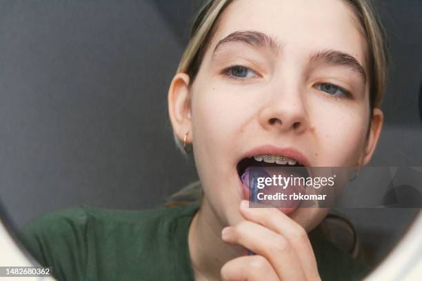 cleaning the tongue with a dental spoon - young woman observes oral hygiene in front of a mirror - mouth hygiene brush stock pictures, royalty-free photos & images