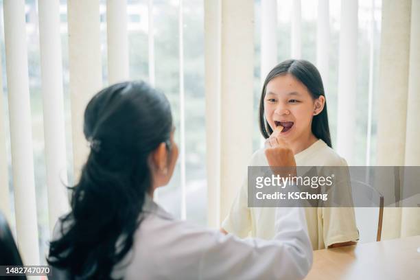 asian indian doctor checking  girl's throat in his office. - girl tongue doctor stockfoto's en -beelden