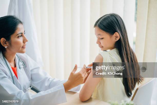 asian indian male doctor performs a vaccination of a girl. - pediatric nurse stock pictures, royalty-free photos & images