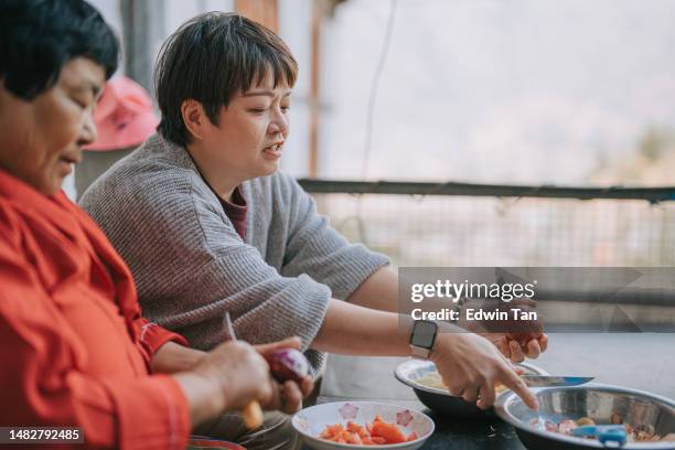 asian chinese female tourist experiential travel cutting potato in bhutanese farmhouse preparing food for dinner with bhutanese senior woman - experiential vacations stock pictures, royalty-free photos & images