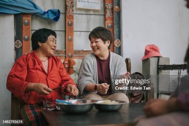 asian chinese female tourist experiential travel cutting potato in bhutanese farmhouse preparing food for dinner with bhutanese senior woman - experiential vacations stock pictures, royalty-free photos & images
