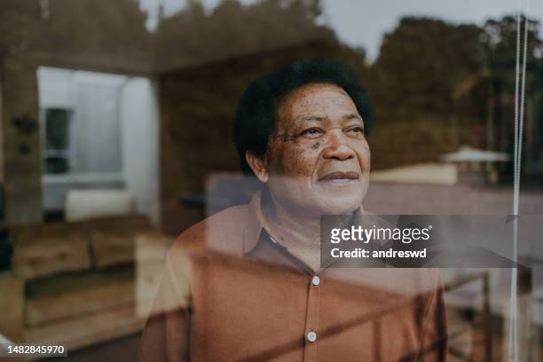 portrait of a senior man looking through the window glass - person looking through window stock pictures, royalty-free photos & images