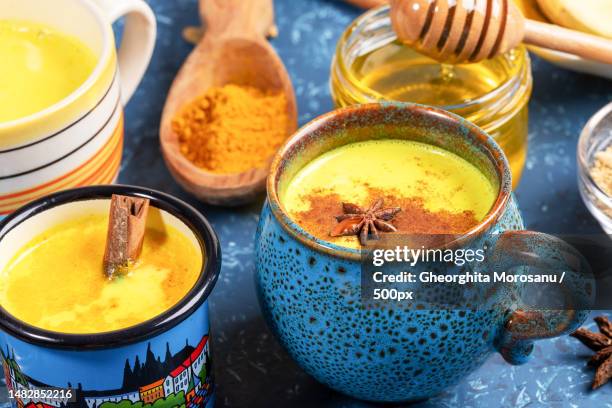 different cups with golden turmeric milk,curcuma powder and honey on blue textured backdrop close,romania - cardamom - fotografias e filmes do acervo