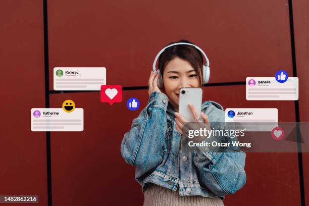 young asian woman wearing headphones on social media with smartphone - generation z icons stock pictures, royalty-free photos & images