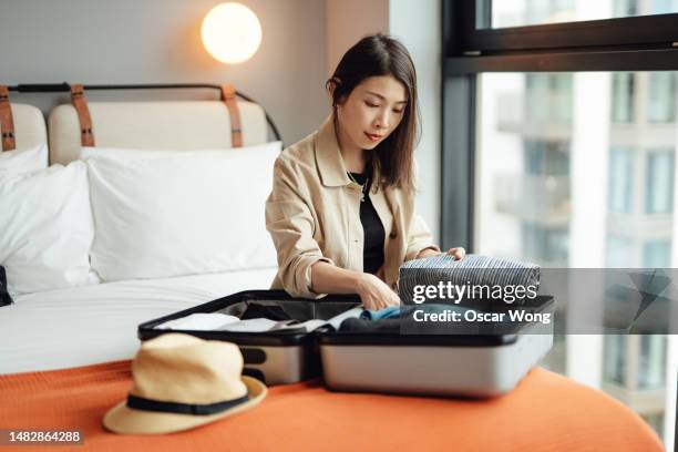 young asian woman unpacking suitcase in the hotel room - asian man suite stock-fotos und bilder