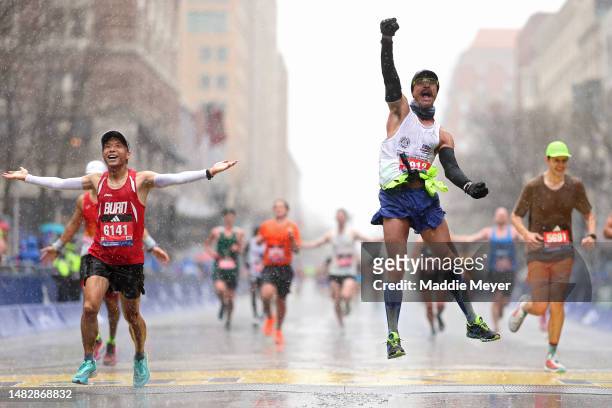 Fernando Ferreira celebrates in the rain as he crosses the finish line next to Zhenfei Lu during the 127th Boston Marathon on April 17, 2023 in...