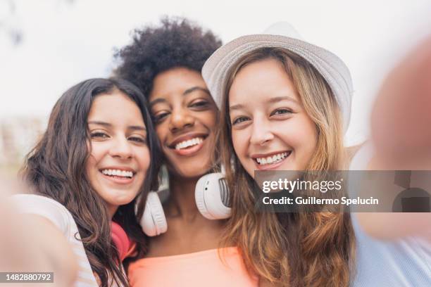 frontal view of three multiethnic friends taking a selfie - close up of beautiful young blonde woman with black hat stock pictures, royalty-free photos & images