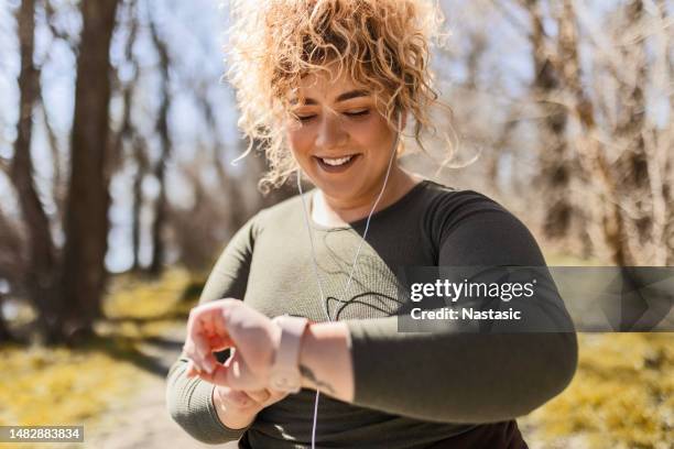 young overweight woman runner with headphones looking at smart - overgewicht stockfoto's en -beelden