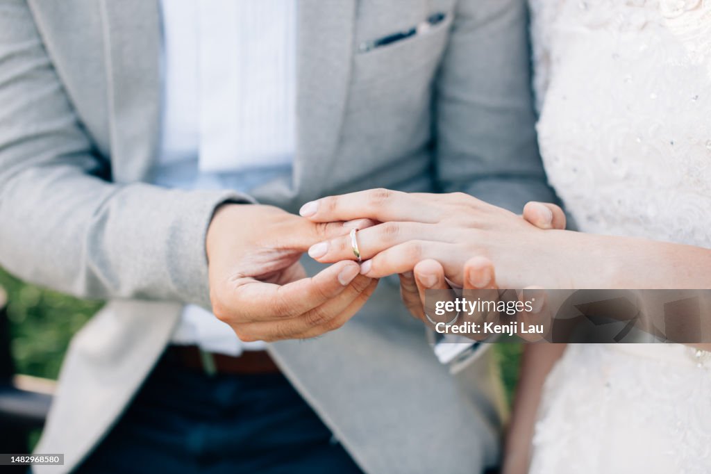 Groom putting ring on bride's finger. Rings exchange. Happy couple celebrating wedding outdoors.