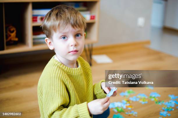 portrait of a 5 year old boy who looking at the camera and holds a piece of the puzzle in his hands, trying to put it together. - mittig stock-fotos und bilder