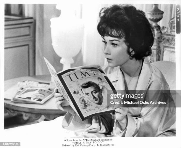 Shirley MacLaine reading Time Magazine with Robert Mitchum on the cover in a scene from the film 'What A Way to Go!', 1964.