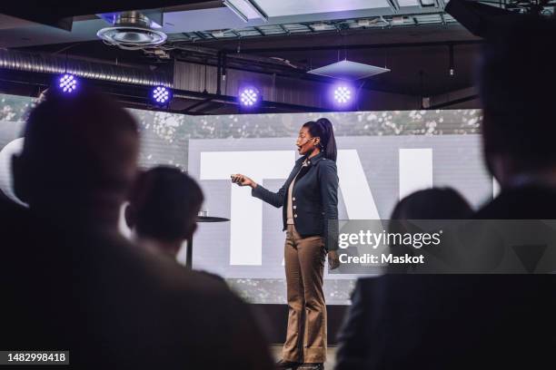 female public speaker with remote controller giving speech at tech event - conference stage stock-fotos und bilder