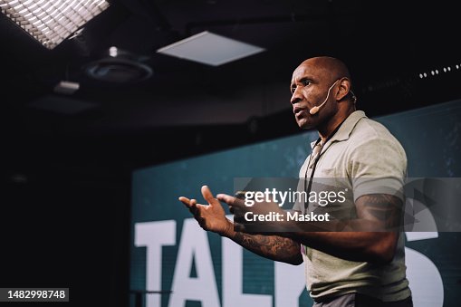 Serious male public speaker gesturing while giving speech at tech event