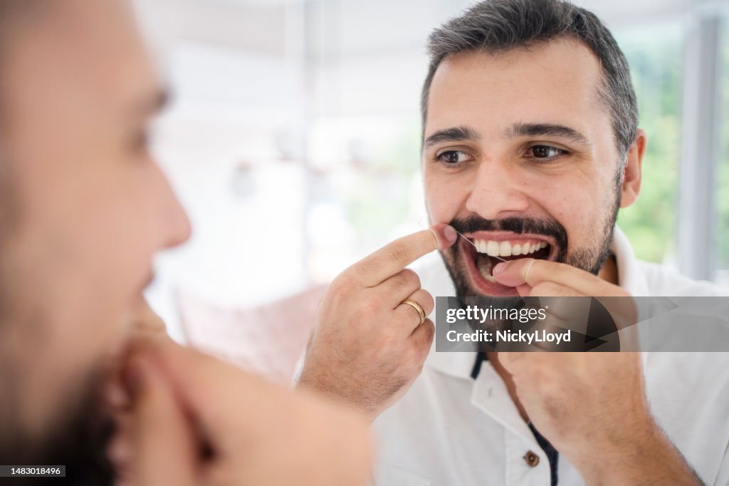 Man flossing his teeth in the mirror of a dentist's office