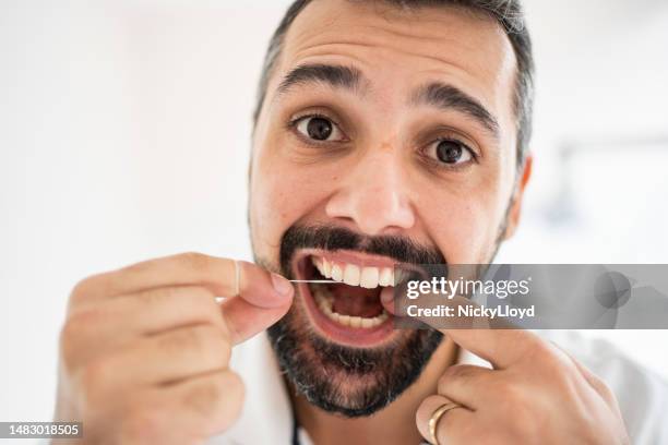 man flossing his teeth in a dentist's office - gingivitis stock pictures, royalty-free photos & images