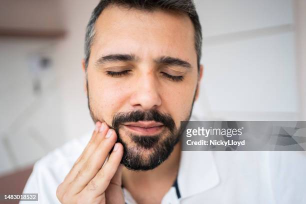 young man with his eyes closed holding his mouth from a toothache - gingivitis stock pictures, royalty-free photos & images